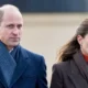 Britain's Prince William and Kate in formal attire smile while standing in front a curtain